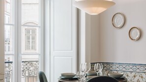 A dining area with a table set for two, a hanging light fixture, and a view of a building through a window. - Ando Living - Madalena House - 101 (Lisboa)
