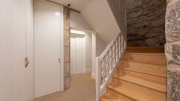 Una escalera con escalones de madera y barandillas blancas que conduce a una habitación con pared de piedra y una puerta con cerradura.