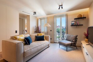 Uma sala de estar moderna com sofá, poltrona e televisão. Há uma varanda com vista para edifícios.