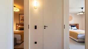 Une chambre d’hôtel avec une porte à deux battants, un lit avec une tête de lit, une table de chevet et un luminaire fixé au mur.
