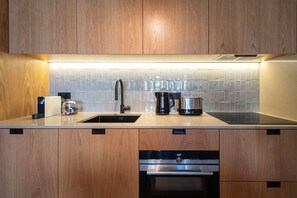 Eine moderne Küche mit Holzschränken, einer Edelstahl-Spüle, einer Kaffeemaschine und einem Geschirrspüler.