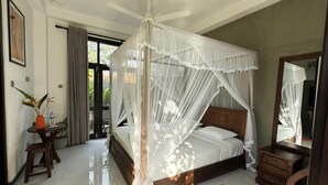 A bedroom with a four-poster canopy bed, a wooden nightstand, a mirror, and a small table with a water bottle and plant. - PRIIMA (Ahangama)