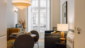 Ett modernt vardagsrum med en soffa, ett matbord med stolar, en lampa och utsikt över staden genom stora fönster.
