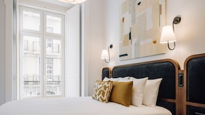 Ett hotellrum med en stor säng, utsikt över byggnader genom ett fönster och en modern, abstrakt målning på väggen.