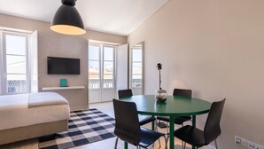 Ein modernes Schlafzimmer mit Bett, einem an der Wand befestigten Fernseher, einem Esstisch mit Stühlen und einem Balkon mit Blick.