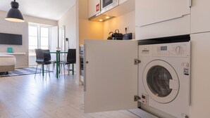 Eine moderne Wohnung mit sichtbarer Waschmaschine, einem Essbereich mit Stühlen und einer Küchenzeile inklusive Mikrowelle.
