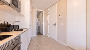 Eine moderne Küche mit Mikrowelle, einem Campingkocher und einem schwarzen Gerät auf der Arbeitsfläche. Der Boden ist aus Holz und ein Flur führt zu einem Badezimmer mit Dusche und Toilette.