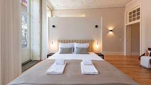 A modern hotel room with a large bed, two bedside lamps, and a view of the city through the window. - Ando Living - Flores 200 Townhouse - 301 (Porto)