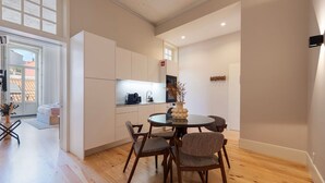 A modern kitchen with white cabinets, a round dining table, and wooden flooring. - Ando Living - Flores 200 Townhouse - 301 (Porto)