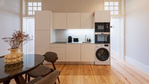 A compact kitchen with a washing machine, microwave, and a small dining area with a table and chairs. - Ando Living - Flores 200 Townhouse - 301 (Porto)