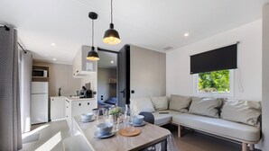 A modern kitchen with a dining area, a sofa, and a window with a view. - “Riviera 48” Mobile Home with Shared Pool, Communal Terrace, and Wi-Fi (Saint-Gervais)
