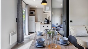 A modern kitchen with a microwave, stove, and sink. There is a dining table set with bowls and glasses. - “Riviera 48” Mobile Home with Shared Pool, Communal Terrace, and Wi-Fi (Saint-Gervais)