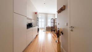 A modern kitchen with white cabinets, a washing machine, and a dining area with a chair and table. - Ando Living - Flores 200 Townhouse - 302 (Porto)