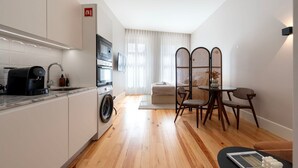 A modern apartment with a kitchen, dining area, and living space. It includes a washing machine, a coffee machine, a dining table with chairs, and a sofa. - Ando Living - Flores 200 Townhouse - 302 (Porto)