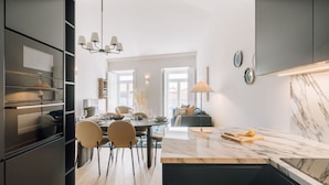 A modern kitchen with a marble countertop, a dining area with chairs, and a view to a balcony. - Ando Living - Abrantes 50 House - 504 (Lisbon)