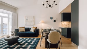 Un salon moderne avec un canapé bleu foncé, une table de salle à manger ronde mise avec des assiettes et des verres, un lampadaire et un lustre.