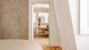 Ein Schlafzimmer mit Bett, Holzboden und Blick auf ein Badezimmer mit Waschbecken und Spiegel.
