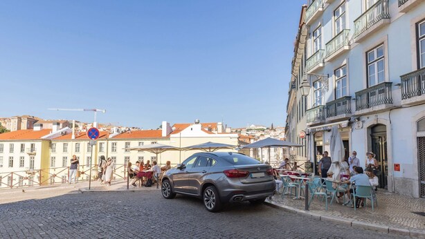 A cobblestone street with a parked car, outdoor seating at a café, and historic buildings with balconies. - Carmo 43 | Apartment 400 (Lisboa)