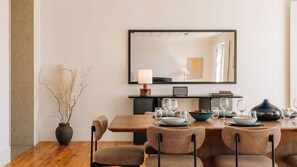 A dining area with a wooden table, four chairs, a vase with dried plants, a lamp, and a mirror on the wall. - Ando Living - Corpo Santo House - 401 (Lisboa)