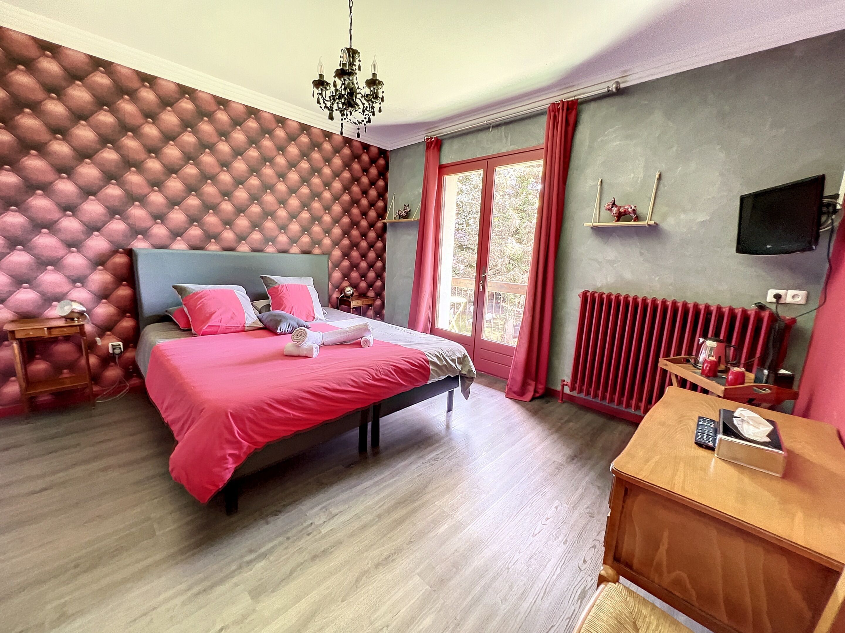 A bedroom with a bed, a wooden nightstand, a desk, a radiator, and a television on the wall.