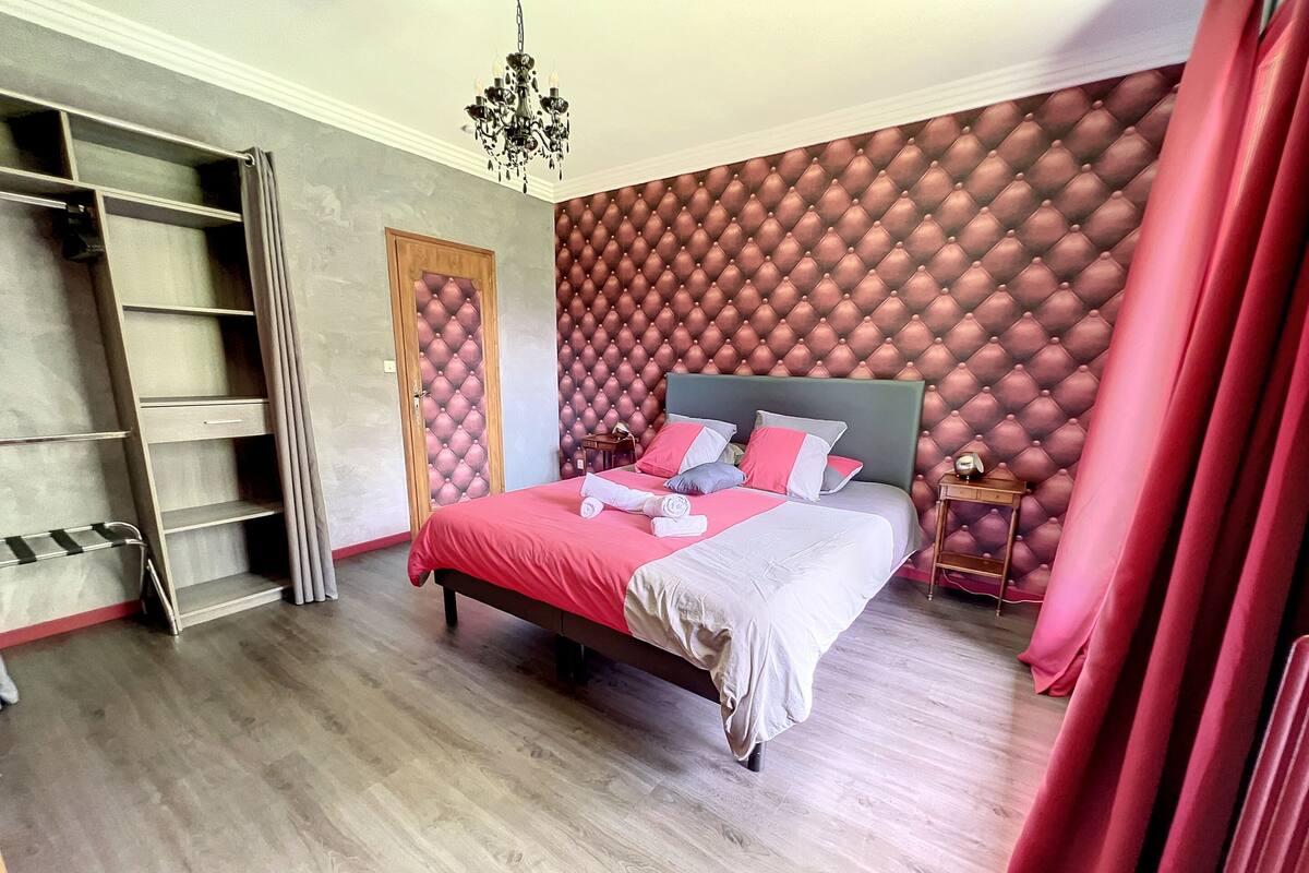 A bedroom with a bed, a wardrobe, a chandelier, and a red curtain.