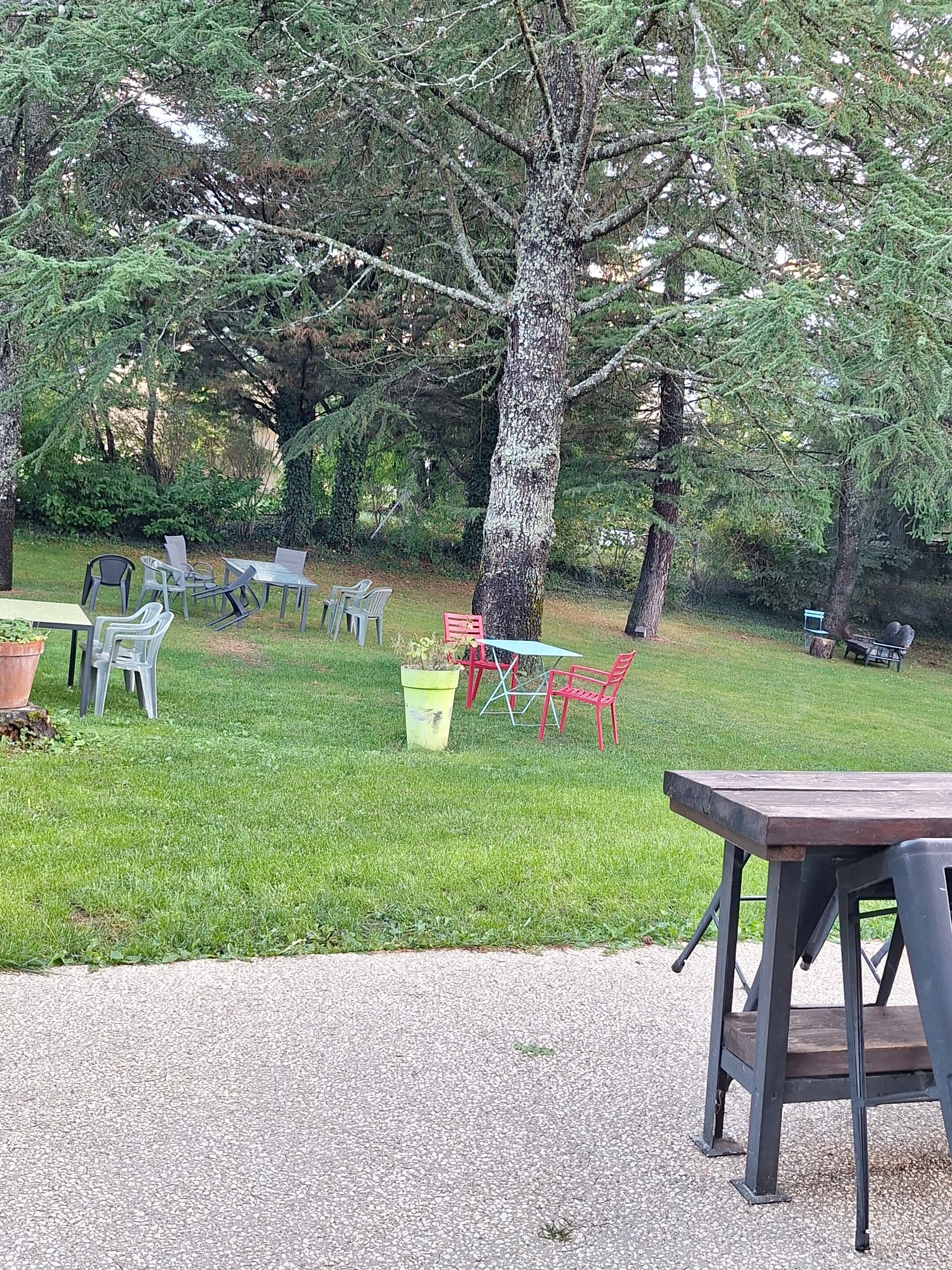 An outdoor seating area with tables and chairs, surrounded by trees and greenery.