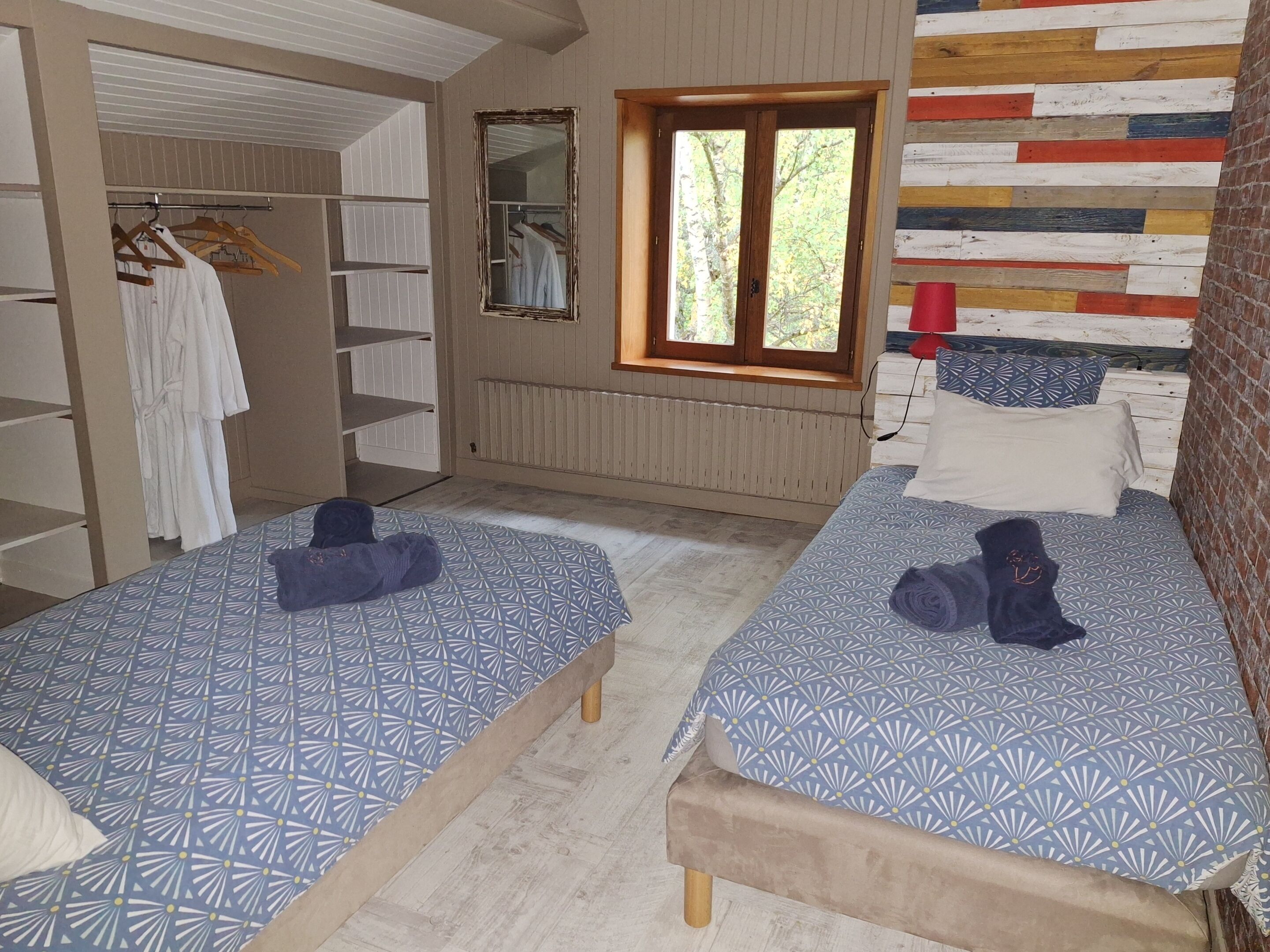 Una habitación con dos camas, un armario, un espejo y una ventana con vistas a árboles.