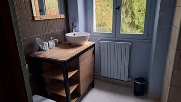 Un baño moderno con tocador de madera, lavamanos blanco y ventana con vistas a árboles.