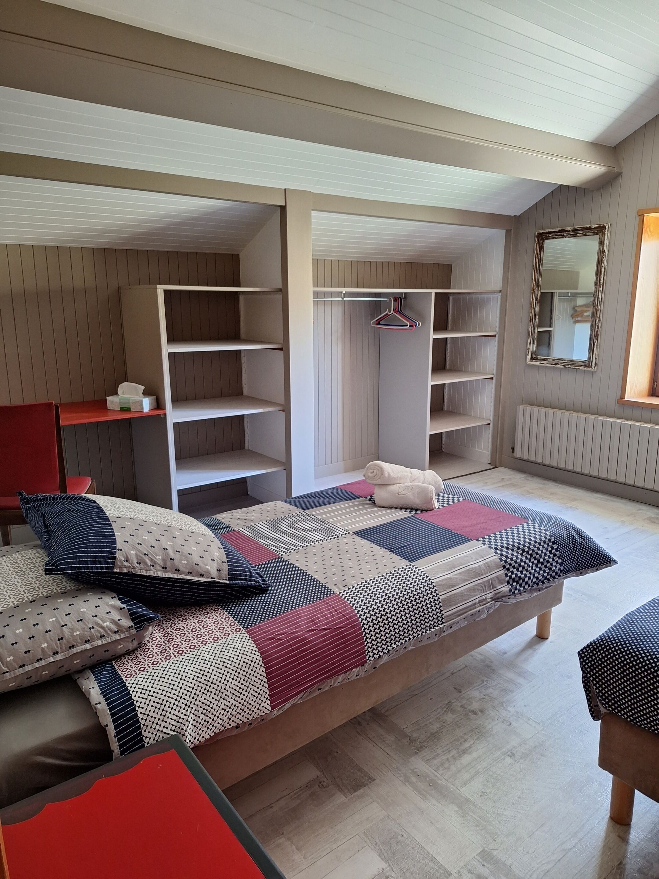 Un dormitorio con una cama, una silla roja, un armario y un espejo.
