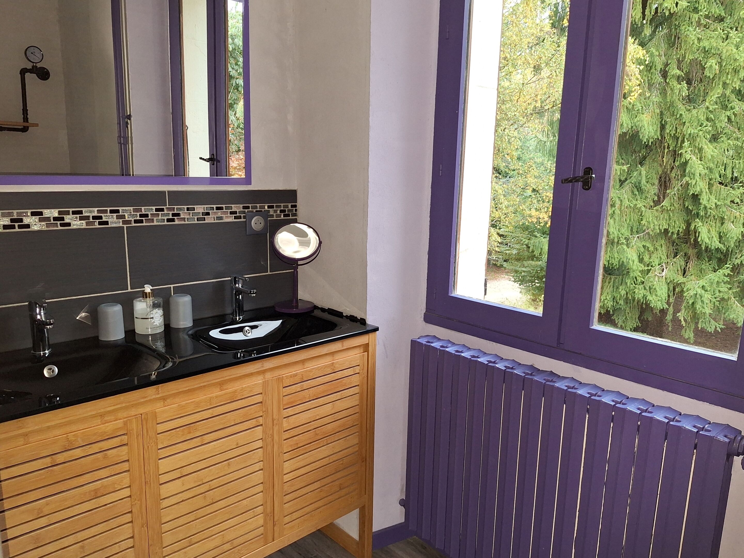 Ein Badezimmer mit einem schwarzen Waschbecken, Holzausbau, einem Spiegel und einem Fenster mit Blick auf Bäume.