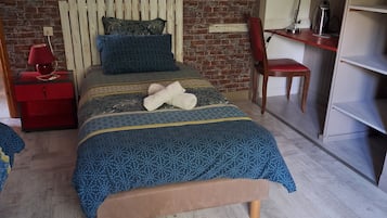 Un dormitorio con pared de ladrillo, cabecera de madera, cama con colcha azul estampada, mesita de noche roja y un escritorio con silla.