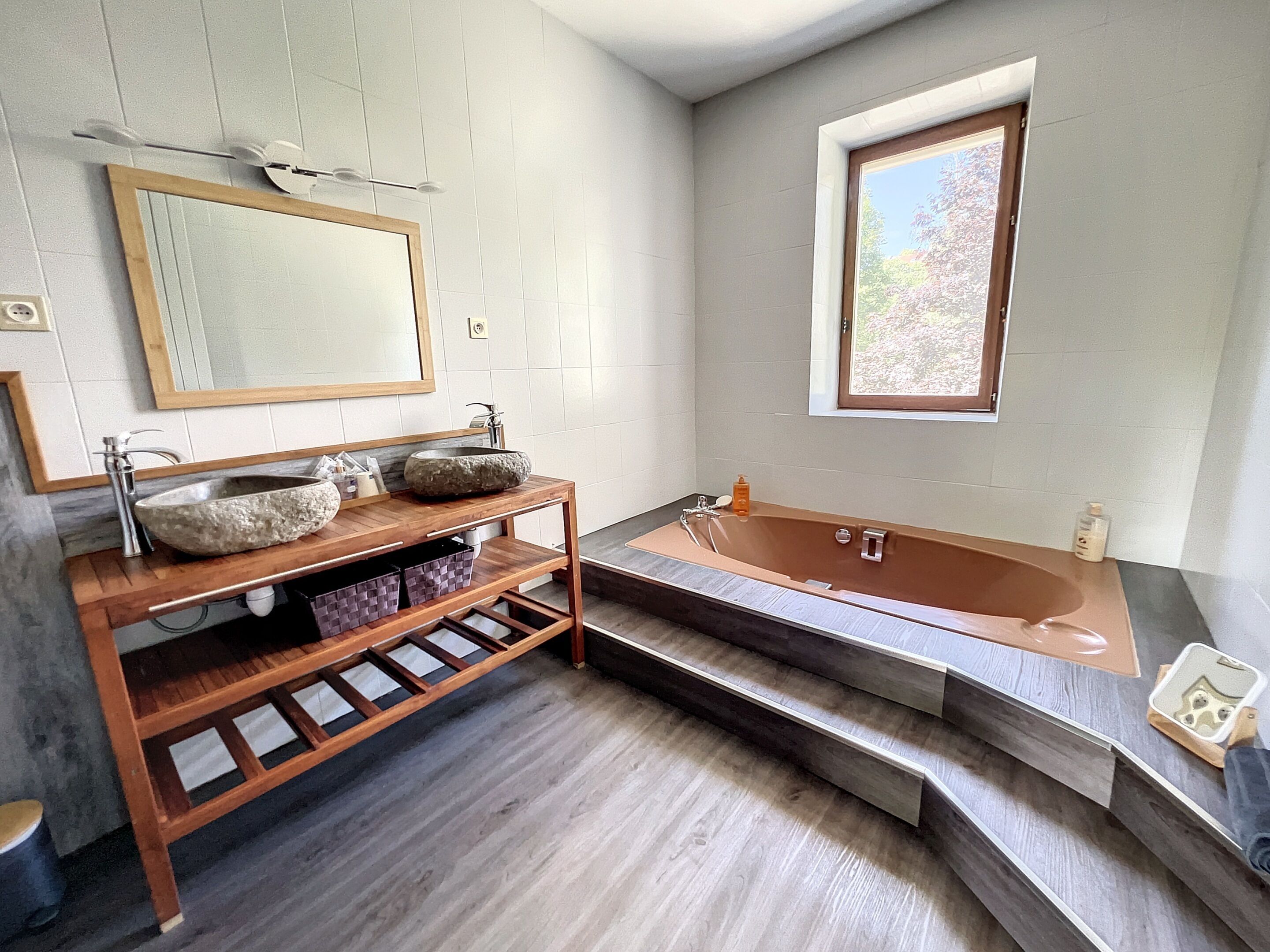 Ein modernes Badezimmer mit einem Steinsink, einem Holzwaschtisch und einer freistehenden Badewanne.