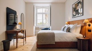 A modern bedroom with a large bed, bedside tables with lamps, a desk with a chair, and a window with a view of buildings. - Ando Living - Corpo Santo House - 302 (Lisboa)
