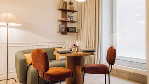 A dining area with a round table set for two, a sofa with two chairs, and a lamp. - Ando Living - Flores 25 House - 002 (Encarnação)