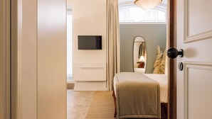 A bedroom with a bed, a TV, a mirror, and a door. - Ando Living - Flores 25 House - 002 (Encarnação)