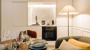A modern kitchen with white cabinetry, a built-in oven, and a dining area with a table set for a meal. - Ando Living - Flores 25 House - 002 (Encarnação)