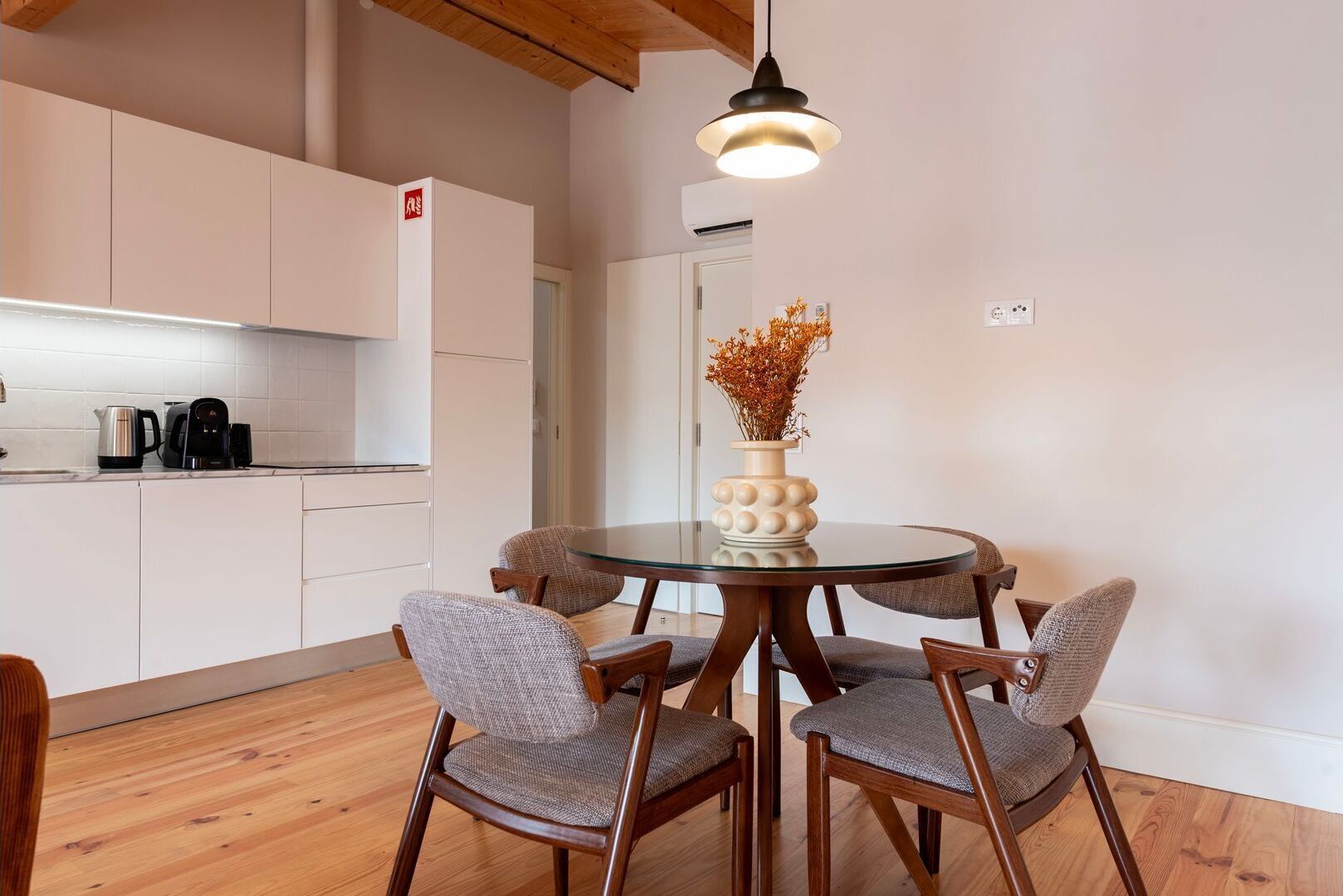 Una cocina moderna con armarios blancos, una mesa redonda de vidrio y sillas de madera.