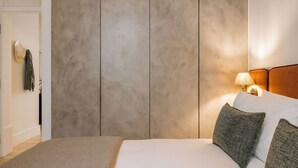 A bedroom with a large bed, a nightstand with a lamp, and a wardrobe with a mirror. - Ando Living - Corpo Santo House - 203 (Lisboa)