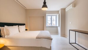 A bedroom with a bed, bedside lamp, window, and a small table. - Carmo 43 | Apartment 403 (Lisboa)