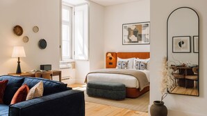 A modern bedroom with a bed, a sitting area with a sofa, a dining table, and a large mirror. - Ando Living - Corpo Santo House - 202 (Lisboa)
