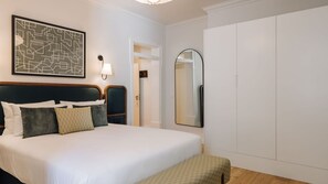 Ein ordentlich eingerichtetes Schlafzimmer mit einem großen Bett, einem Nachttisch, einer Wandlampe, einem Spiegel und einem Kleiderschrank.