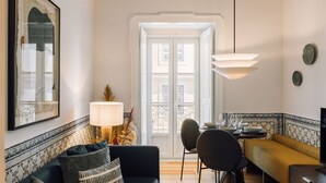 A modern living room with a sofa, a dining table with chairs, a lamp, and a framed artwork on the wall. - Ando Living - Madalena House - 402 (Lisboa)