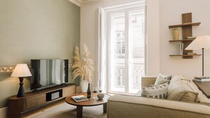 Een woonkamer met een flatscreen televisie, een salontafel, een bank, een lamp en een boekenkast.
