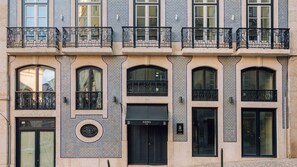 Ein Gebäude mit mehreren Balkonen, großen Fenstern und einer auffälligen schwarzen Tür mit der Aufschrift 'ANDO Living'.