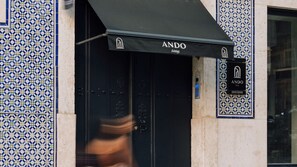 A building facade with a patterned tile design and a black awning with the name "ANDO" and the word "Living". - Ando Living - Madalena House - 501 (Lisboa)