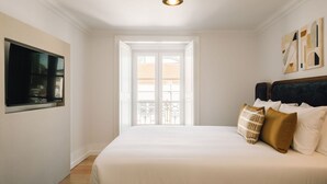 A bedroom with a large bed, a TV mounted on the wall, and a view through a window. - Ando Living - Madalena House - 501 (Lisboa)