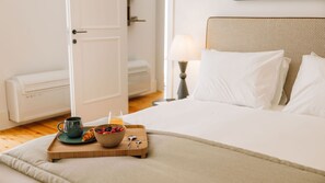 Una cama bien tendida con sábanas blancas, una bandeja de madera con alimentos para el desayuno y una lámpara de noche.