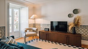 Ein Wohnzimmer mit Sofa, Sessel, Fernseher auf einem Holzschrank, Lampe und dekorativen Tellern an der Wand.