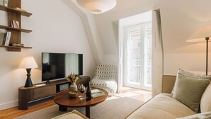 Una sala moderna con televisor de pantalla plana, una mesa de centro con un florero y copas de vino, un sofá, una silla y una estantería.