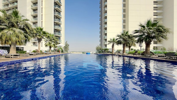 A swimming pool surrounded by palm trees and modern high-rise buildings. - Stylish 1BR Apartment at Golf Gate (Dubai)